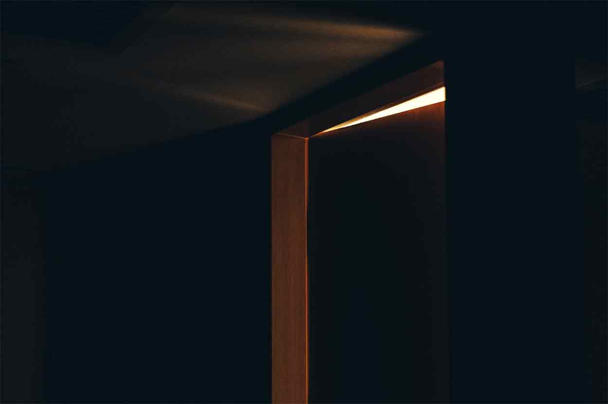 A door just starting to open, letting light into a dark room.