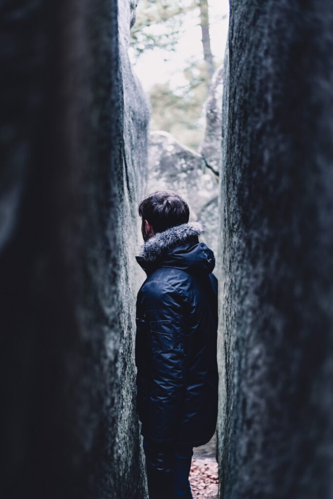 Man passing through a very narrow gap between two stone walls.