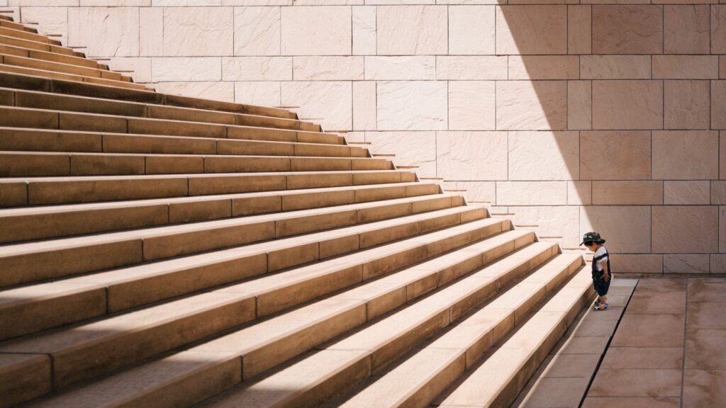 Small boy standing at the bottom of a huge staircase.